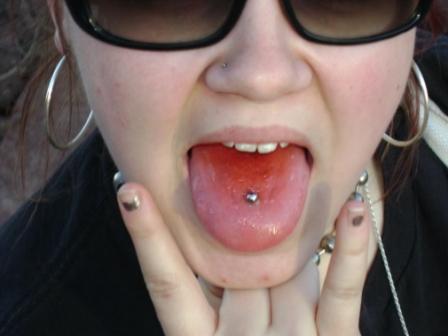Close up of a young woman in black shades with her tongue and ear piercings