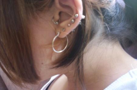 A women showing her lobe, tragus and four other ear piercings.