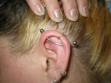 A blonde removing her hairs from her ear to showcase her ear piercing.