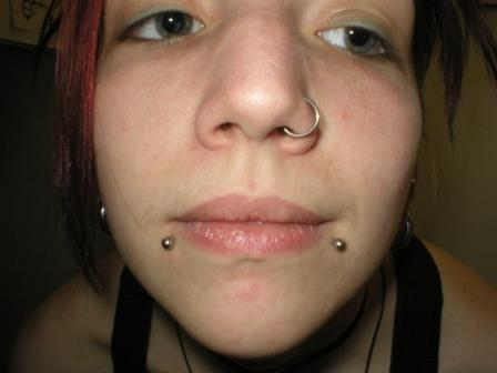A red haired girl giving close look of her sanke bites and nose piercing.