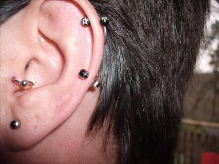 A guy showing his tragus, lobe, helix and outer conch ear piercings.