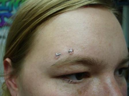 Close look of barbell pierced just above the right eyebrow of a girl.