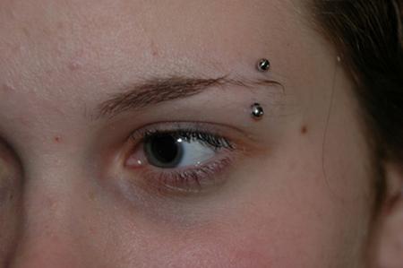 Close look of barbell pierced in left eyebrow of a girl